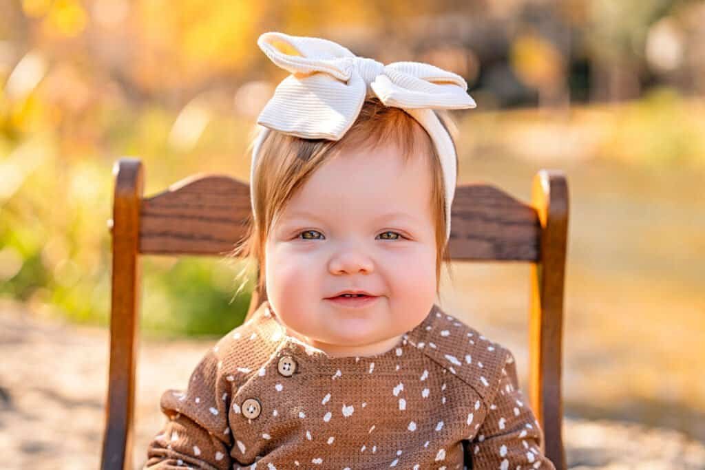 Adorable toddler girl with a bow headband enjoying a sunny fall day outdoors.