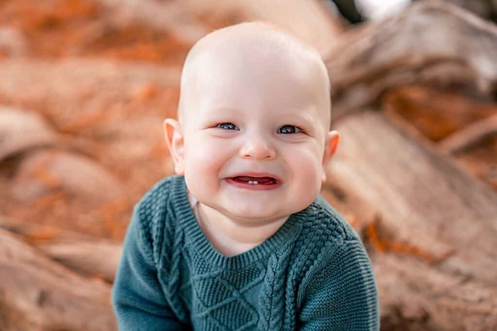 Close-up of smiling baby with blue eyes and missing front teeth, outdoor natural background.