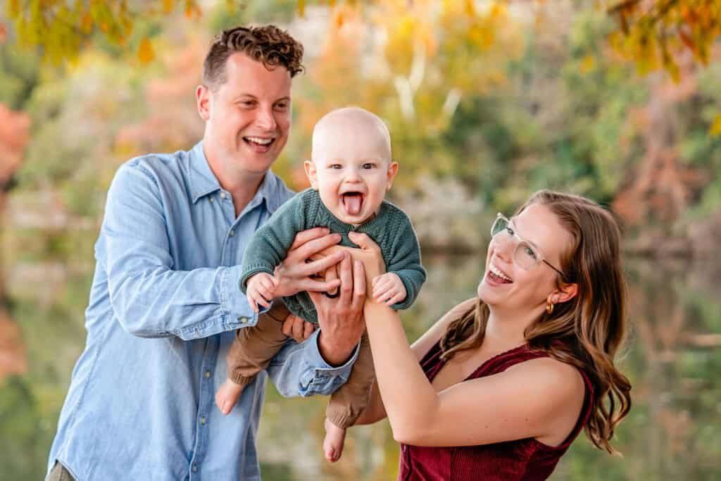Happy family enjoying fall outdoors with adorable baby, vibrant autumn leaves in background.