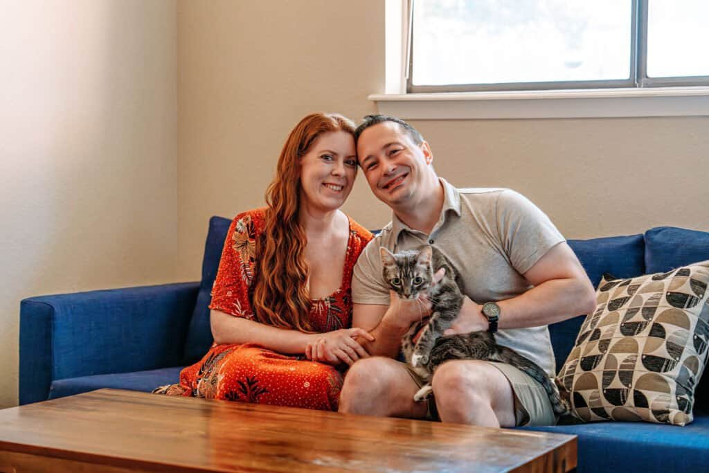 A couple posing for photos with their cat in their Austin home before their move
